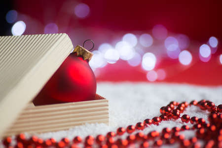 Red Christmas ball in open box with beads and garland lights on bokeh background. New year banner with copy space. Concept of Xmas gift.の写真素材