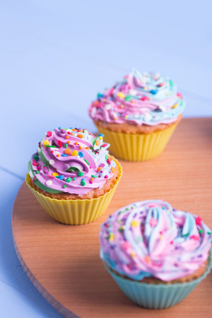 Closeup different colorful cupcakes decorated with sprinkles on wooden round desk. Multicolored...