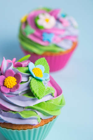 Closeup two cupcakes creamy multicolored top decorated with colorful flowers and leaves on blue background. Spring cake for Motherâs or Women day.の写真素材