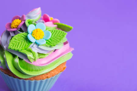Closeup cupcake creamy multicolored top decorated with colorful flowers and leaves on purple background. Spring cake for Motherâs or Women day.の写真素材