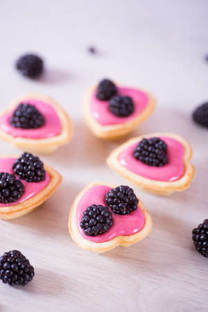 Closeup pink berry yogurt decorated with blackberries in five heart-shaped tartlets. Tender female romantic dessert.の写真素材