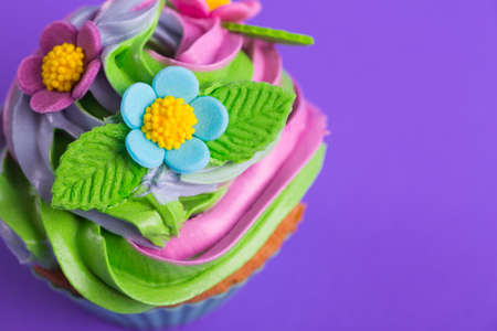 Closeup cupcake creamy multicolored top decorated with colorful flowers and leaves on purple background. Spring cake for Motherâs or Women day.の写真素材