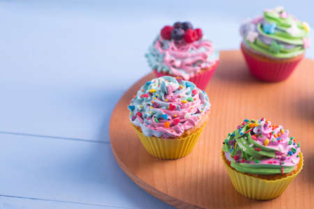 Closeup different colorful cupcakes decorated with sprinkles on wooden round desk. Multicolored pastel desserts.の写真素材
