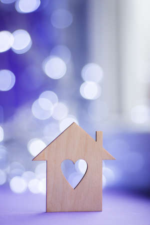 Wooden icon of house with hole in the form of heart on near window in daylight with bokeh lights on blurred purple background. Romantic card with copy space. Concept of sweet home.の写真素材