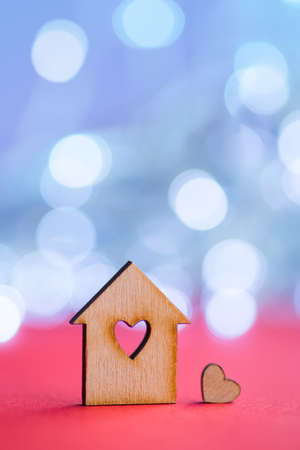 Wooden icon of house with hole in the form of heart with little heart on red table with light bokeh background. Romantic card with copy space. Concept of sweet home.の写真素材