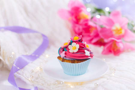 Closeup cupcake with creamy multicolored top decorated with colorful flowers with pink tulips, bokeh lights and satin ribbon on blurred background. Spring cake for Women or Motherâs dayの写真素材