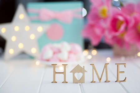 Wooden inscription "Home" with spring pink tulips, glowing LED star and gift box on blurred background with warm bokeh. Concept of sweet home.の写真素材