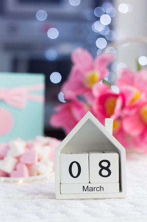 Cute wooden calendar with date of March 8 with beautiful bouquet of tender pink tulips and gift on...
