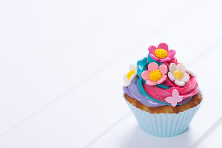 Closeup cupcake with creamy multicolored top decorated with colorful flowers and leaves on white wooden table. Spring cake for Women or Motherâs dayの写真素材