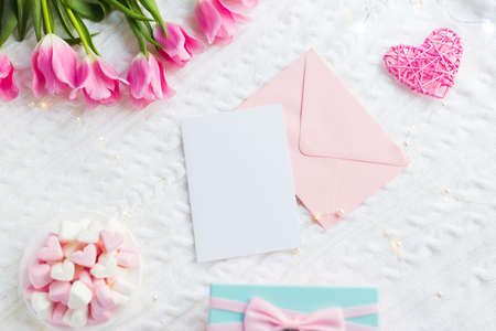 Clear paper and envelope with gift box, pink tulips, heart and marshmallow on white knitted plaid, top view. Card with copy space. Spring romantic composition for text, tender flat lay.の写真素材