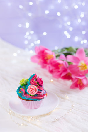 Closeup cupcake with creamy multicolored top decorated with colorful roses with pink tulips, bokeh lights and satin ribbon on blurred background. Spring cake for Women or Motherâs dayの写真素材