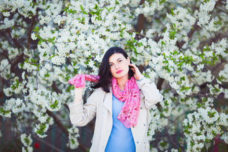 Portrait of young pretty woman in white blooming cherry branches in spring outdoor.