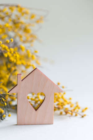 Closeup wooden house with hole in form of heart with yellow mimosa branches on lilac background with copy space. Spring vibrant composition. Concept of sweet home.の写真素材