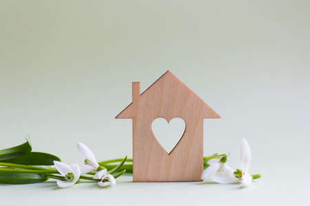 Closeup wooden house with hole in form of heart with tender white snowdrops flowers on light green background with copy space. Spring romantic composition. Concept of sweet home.の写真素材