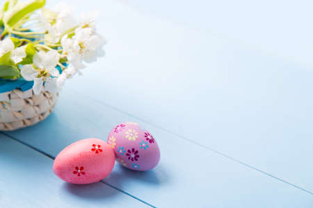 Two painted pink and purple Easter eggs near basket with white spring flowering branch on light blue background.の写真素材
