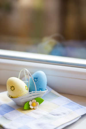 Colorful blue and yellow Easter eggs in basket with decorative flower near window in daylight. Spring home vibrant composition with copy space. Easter in Ukraine.の写真素材