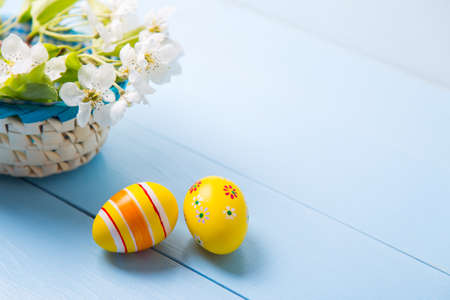 Two painted orange Easter eggs near basket with white spring flowering branch on light blue background.の写真素材