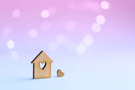 Wooden icon of house with hole in the form of heart with little heart on pastel blurred background with light bokeh. Romantic card with copy space. Concept of sweet home.の写真素材