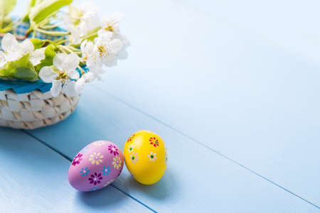 Two painted orange and purple Easter eggs near basket with white spring flowering branch on light blue background.の写真素材