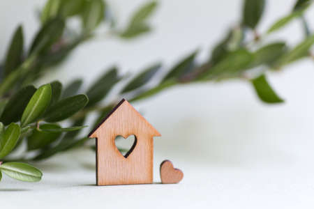 Closeup wooden house with hole in form of heart with green buxus branch on light background with copy space. Ecological natural composition. Concept of eco-house.の写真素材