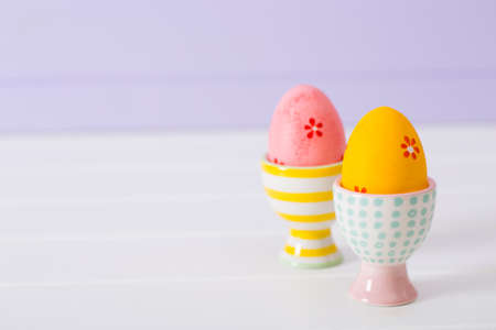 Closeup two colorful painted Easter eggs in vibrant modern egg stands on pastel lilac background. Spring home minimalistic composition with copy space.の写真素材