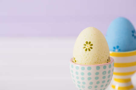 Closeup two colorful painted Easter eggs in vibrant modern egg stands on pastel lilac background. Spring home minimalistic composition with copy space. Easter in Ukraine.の写真素材