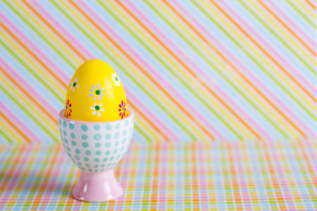 Closeup colorful painted Easter egg in vibrant modern egg stand on striped rainbow background. Spring home minimalistic composition with copy space. Geometric style.の写真素材