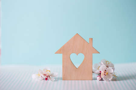 Closeup wooden house with hole in form of heart surrounded by white flowering tree branches on pastel blue background. Spring vibrant composition with copy space. Concept of sweet home.の写真素材