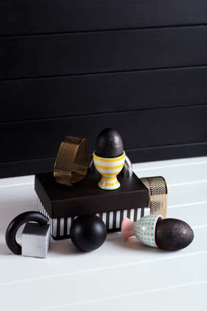 Modern stylish composition with Easter eggs in vibrant egg stands with geometric figures and metallic shapes with different texture on black and white background. Dark minimalistic design with golden and silver elements.の写真素材