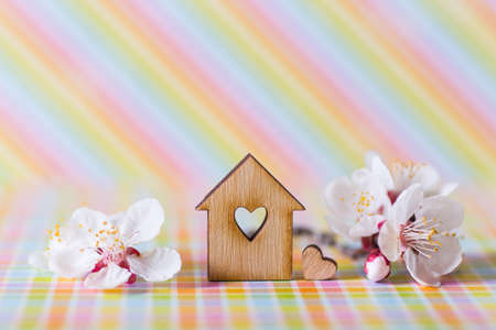 Closeup wooden house with hole in form of heart surrounded by white flowering tree branches on rainbow striped background. Spring vibrant composition with copy space. Concept of sweet home.の写真素材
