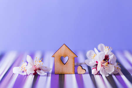 Closeup wooden house with hole in form of heart surrounded by white flowering tree branches on purple background. Spring vibrant composition with copy space. Concept of sweet homeの写真素材