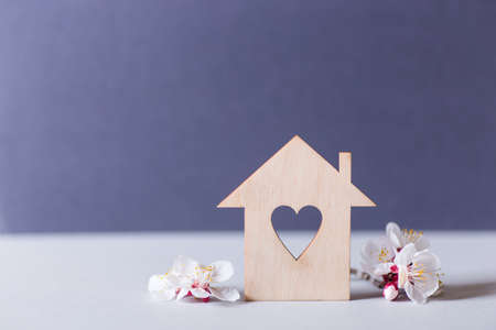 Closeup wooden house with hole in form of heart surrounded by white flowering tree branches on gray background. Spring vibrant composition with copy space. Concept of sweet home.の写真素材