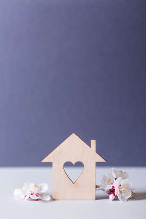 Closeup wooden house with hole in form of heart surrounded by white flowering tree branches on gray background. Spring vibrant composition with copy space. Concept of sweet home.の写真素材