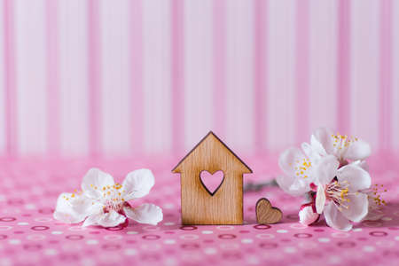 Closeup wooden house with hole in form of heart surrounded by white flowering tree branches on pink striped background. Spring vibrant composition with copy space. Concept of sweet home.の写真素材