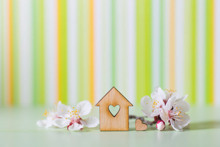 Closeup wooden house with hole in form of heart surrounded by white flowering tree branches on green...