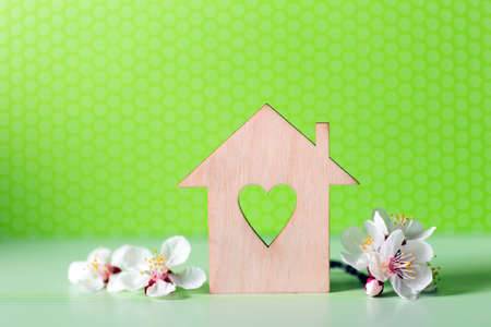 Closeup wooden house with hole in form of heart surrounded by white flowering tree branches on green background. Spring vibrant composition with copy space. Concept of sweet home.の写真素材