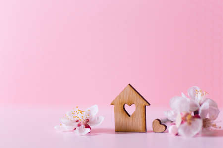 Closeup wooden house with hole in form of heart surrounded by white flowering tree branches on pastel pink background. Spring vibrant composition with copy space. Concept of sweet homeの写真素材