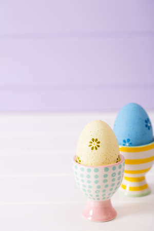 Two colorful painted Easter eggs in vibrant modern egg stands on pastel lilac background. Spring home minimalistic composition with copy space. Easter in Ukraine.の写真素材