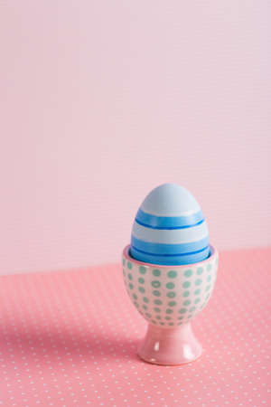 Closeup colorful painted Easter egg in vibrant modern egg stand on pastel pink background. Spring home minimalistic composition with copy space. Geometric style.の写真素材