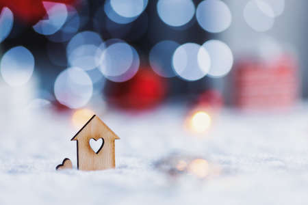 Wooden icon of house with hole in form of heart with red home Christmas decor and blurred bokeh background in daylight. New Year card with copy space. Concept of sweet home.の写真素材
