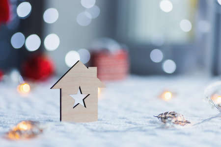 Wooden icon of house with hole in form of star with red home Christmas decor and blurred bokeh background in daylight near window. New Year card with copy space. Concept of holiday at home.の写真素材