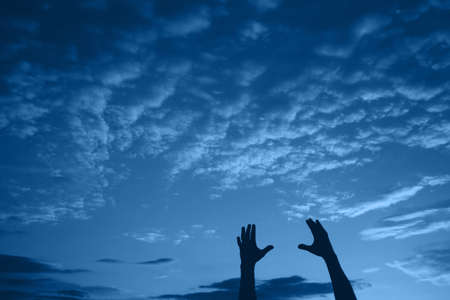 Silhouette of male hands against cloudy sky on evening. Natural banner with color of the year 2020 - Classic Blue. Concept of freedom. Copy space.の写真素材