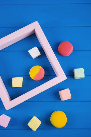 Minimalistic food composition of colorful macaroons and square marshmallow with pink frame on vibrant Classic blue background. Concept of summer dessert, geometric style.の写真素材