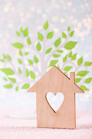Wooden icon of house with hole in form of heart with green tree on white background with bokeh lights. Spring or ecological banner. Concept of sweet home and harmony with nature.の写真素材