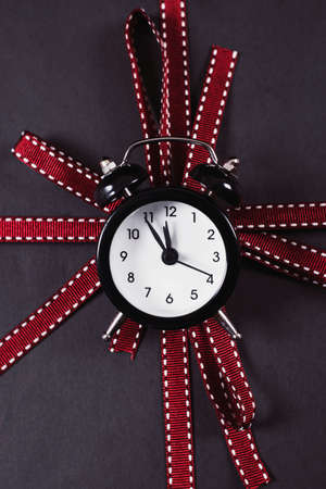 Black and white alarm clock on the top of wrapped gift box with red ribbon, close-up, high angle. Black Friday sale. Concept of shopping time.の写真素材