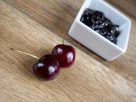 Cherry jam unfocused with two cherries on wood backgroundの写真素材