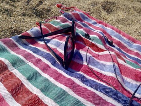 Colorful towel with sunglasses and earphones on the beachの写真素材