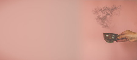 Hand with cup of coffee on pink background with copy space