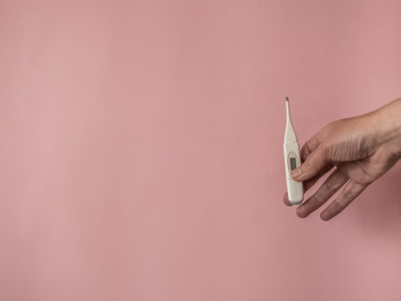 Hand with thermometer on pink background with copy space