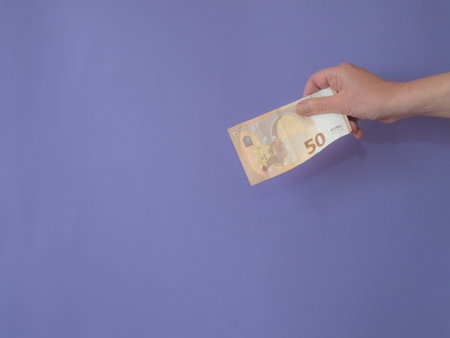 Hand with banknote of fifty euros on purple bankground with copy space